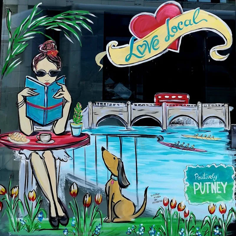 Bespoke hand painted window art of a lady sitting at a table reading a book by Putney Bridge.